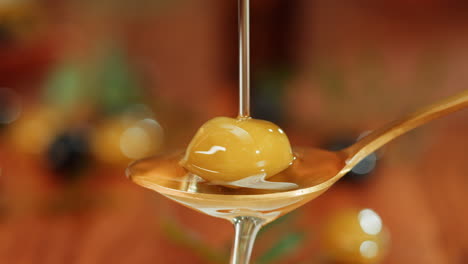 olive oil being poured over an olive on a spoon