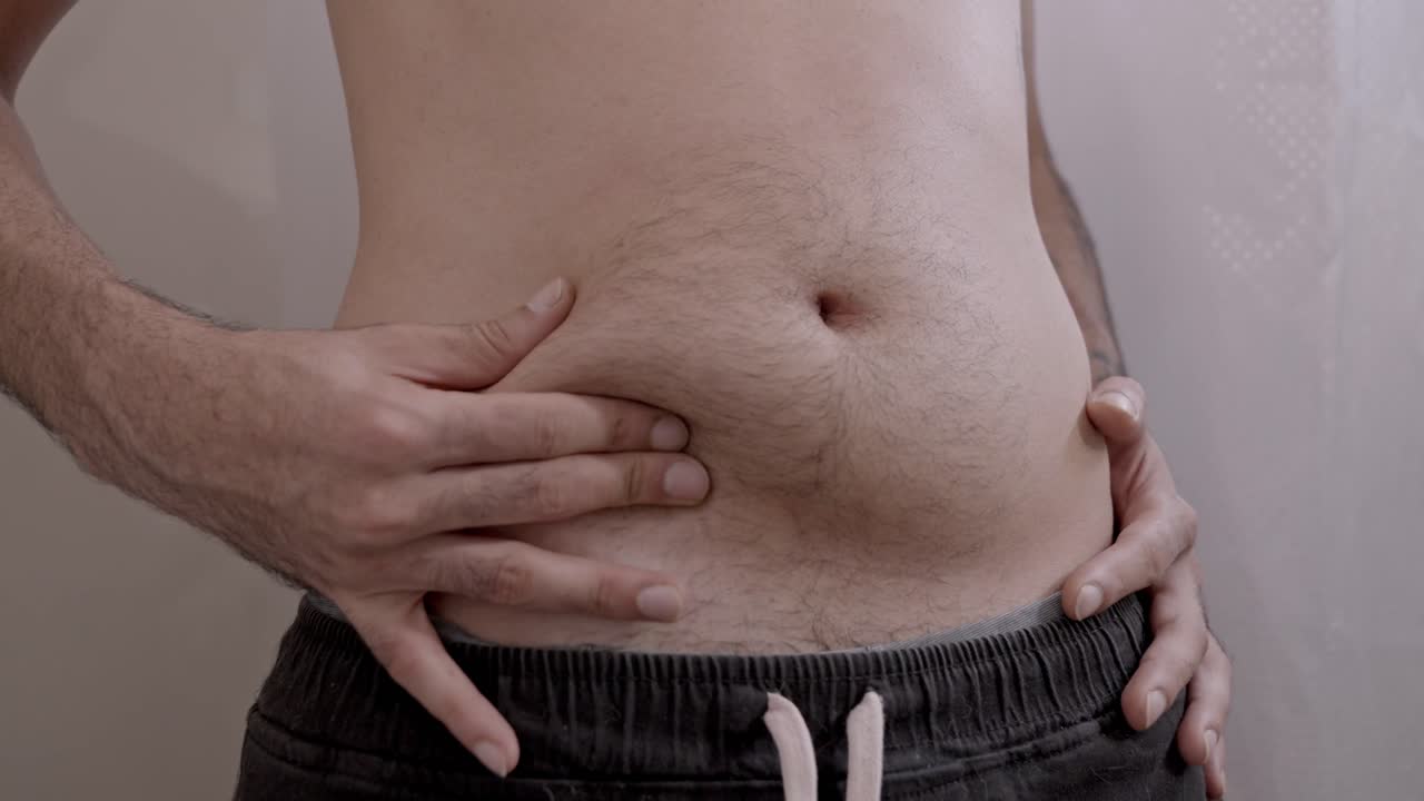 Primo piano di un uomo infelice che controlla il grasso addominale e il suo corpo. Persona triste con problemi di sovrappeso preoccupata per la sua salute e il suo aspetto