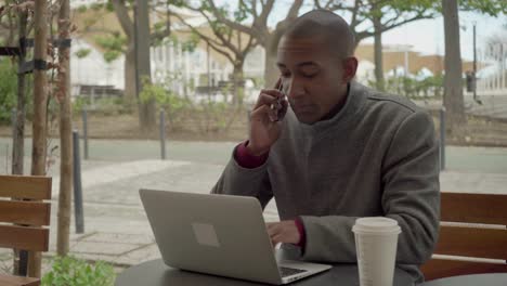 Young-freelancer-using-smartphone-and-laptop-computer-outdoor