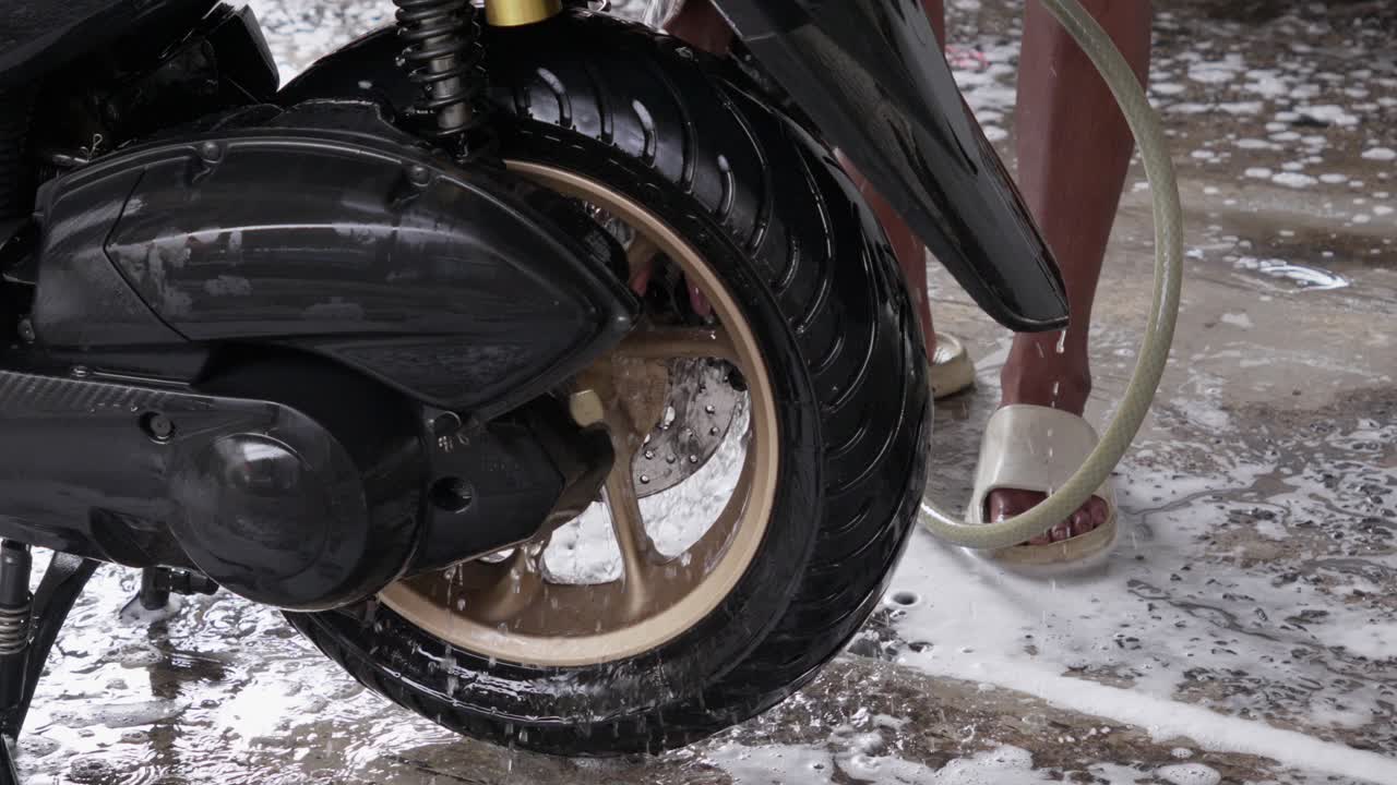 Person Washing and Rinse Motorcycle Wheel With Water Pipe, Soapy Water On Floor