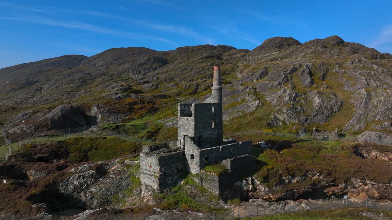 Copper Mine, Allihies, County Cork, Ireland, September 2024. Drone orbits counter clockwise and pulls backwards away from the historic stone Engine House on a mountain slope under a clear blue sky.
