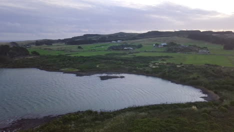 aerial drone footage of farmland along the coast of new zealand at sunset with windmills in the background