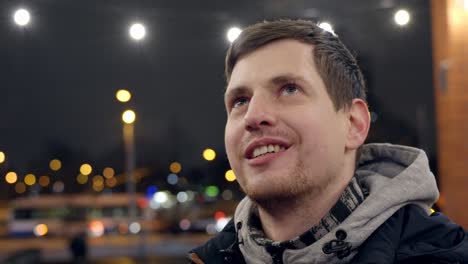 Young-happy-man-smiling-in-city-lights,-gazing-up-in-closeup-ant-talking