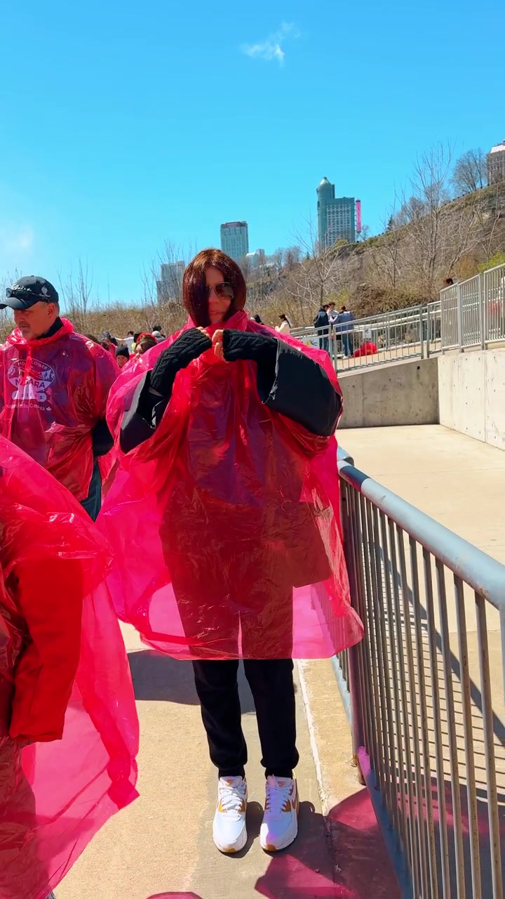 Niagara Falls, Canada, 1 May 2026 : Tourist wrapped in blowing red poncho at Niagara Falls, Canada. Strong wind covers walking person with plastic garment.