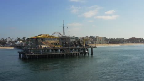 AERIAL:-Reverse-flight-looking-at-Santa-Monica-Pier-in-Los-Angeles,-California,-Sunny,-Blue-Sky