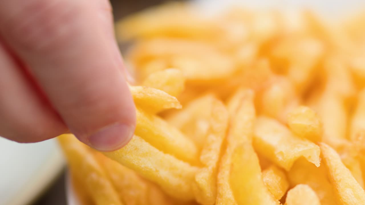 Close-up of hand grabbing golden fries from plate, shallow depth, natural lighting, soft focus
