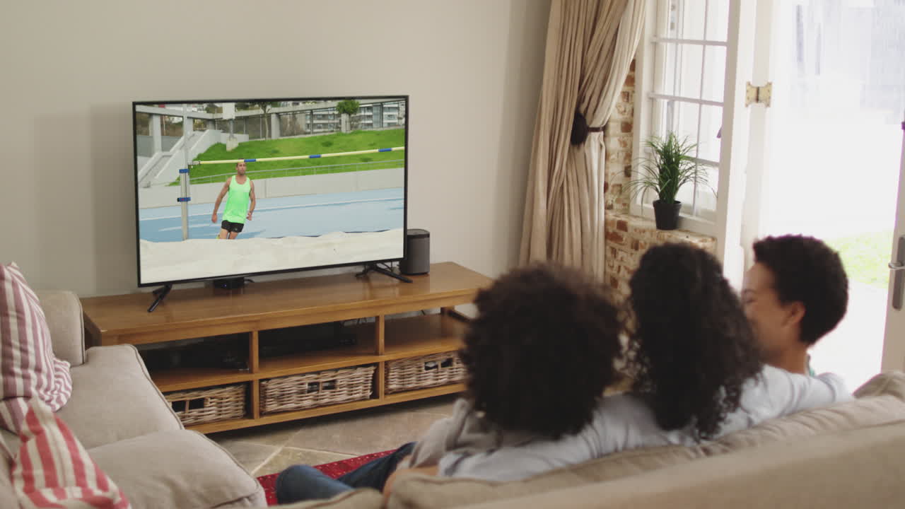 Famiglia felice seduta a casa insieme che guarda l'atletica salto in alto in TV