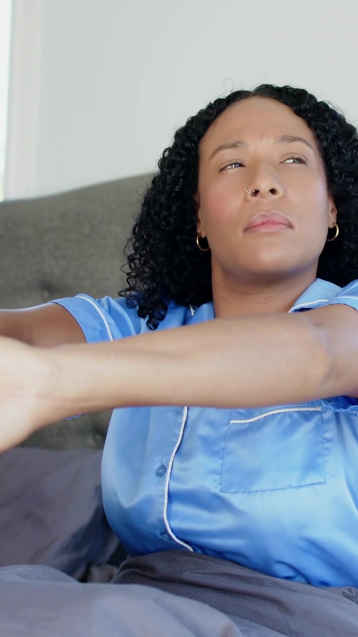 Verticale video: Vrouw in blauwe top opent ogen, wrijft handen, strekt armen in bed en wordt wakker.
