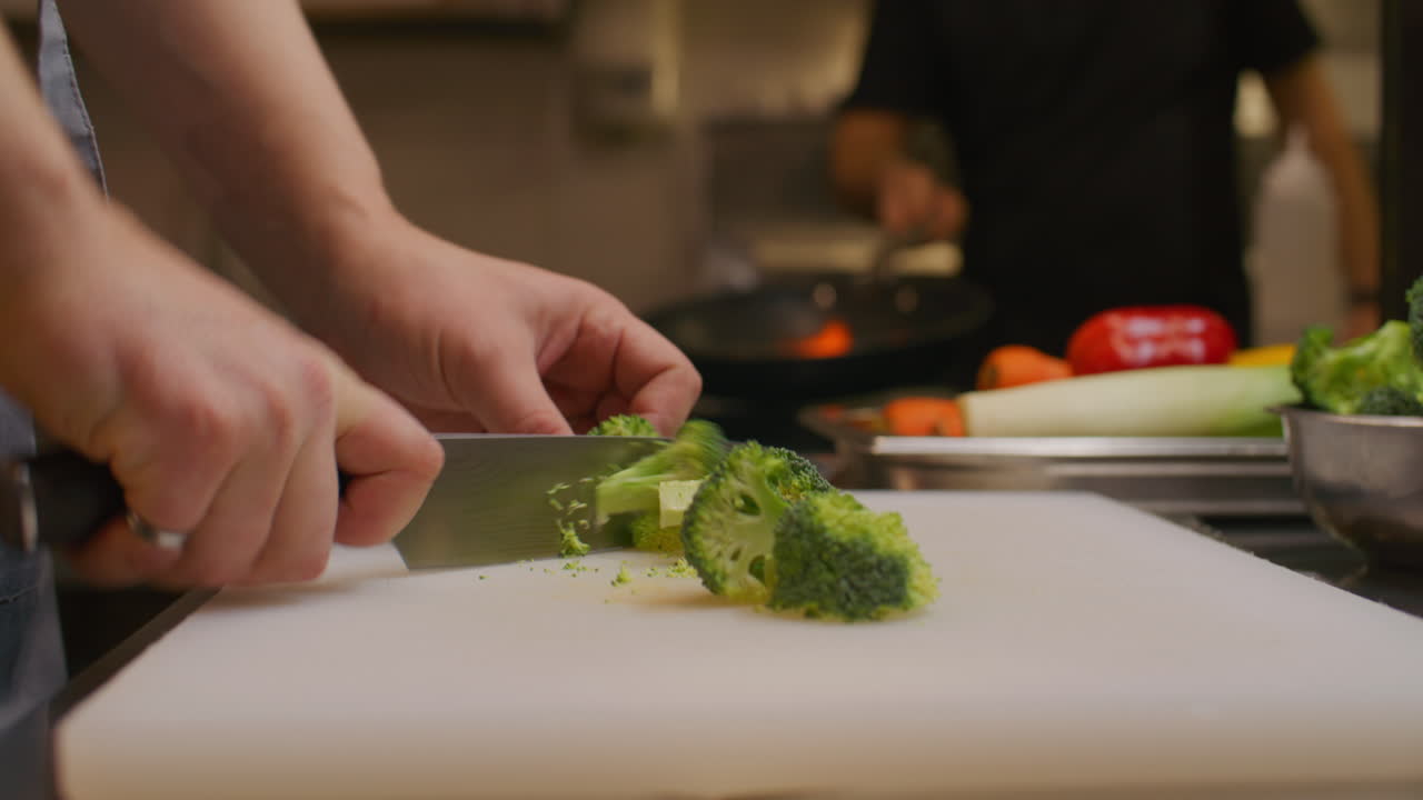 Mani dello chef che affettano broccoli freschi su un tagliere nella cucina di un ristorante