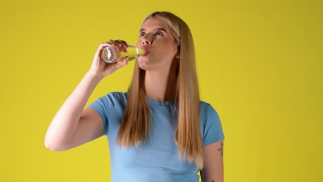 young blonde woman drinking water from glass bottle, studio portrait