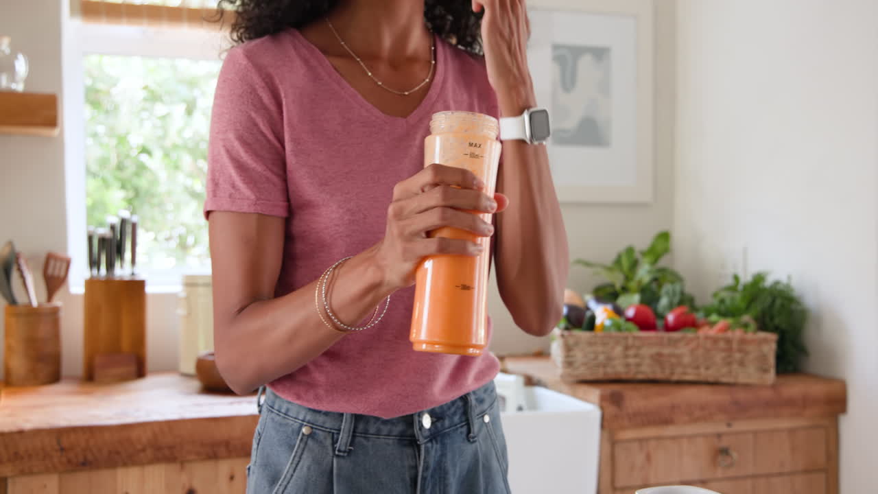 Woman pouring fresh orange juice into glass in bright kitchen, smiling happily, at home