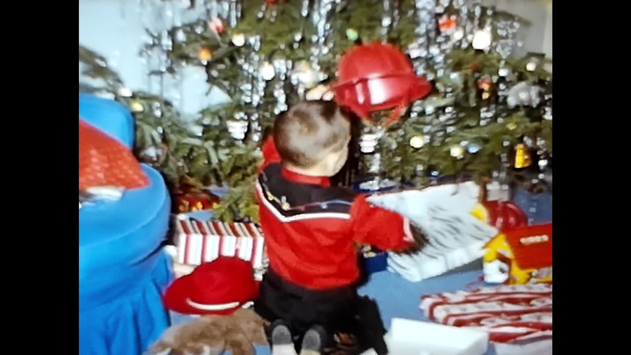 Little Boy in Red Jacket and Hat Standing in Front of Christmas Tree. CIRCA USA - 1970s: A little boy wearing a red jacket and hat stands in front of a Christmas tree in this 1970s video archive from the USA.
