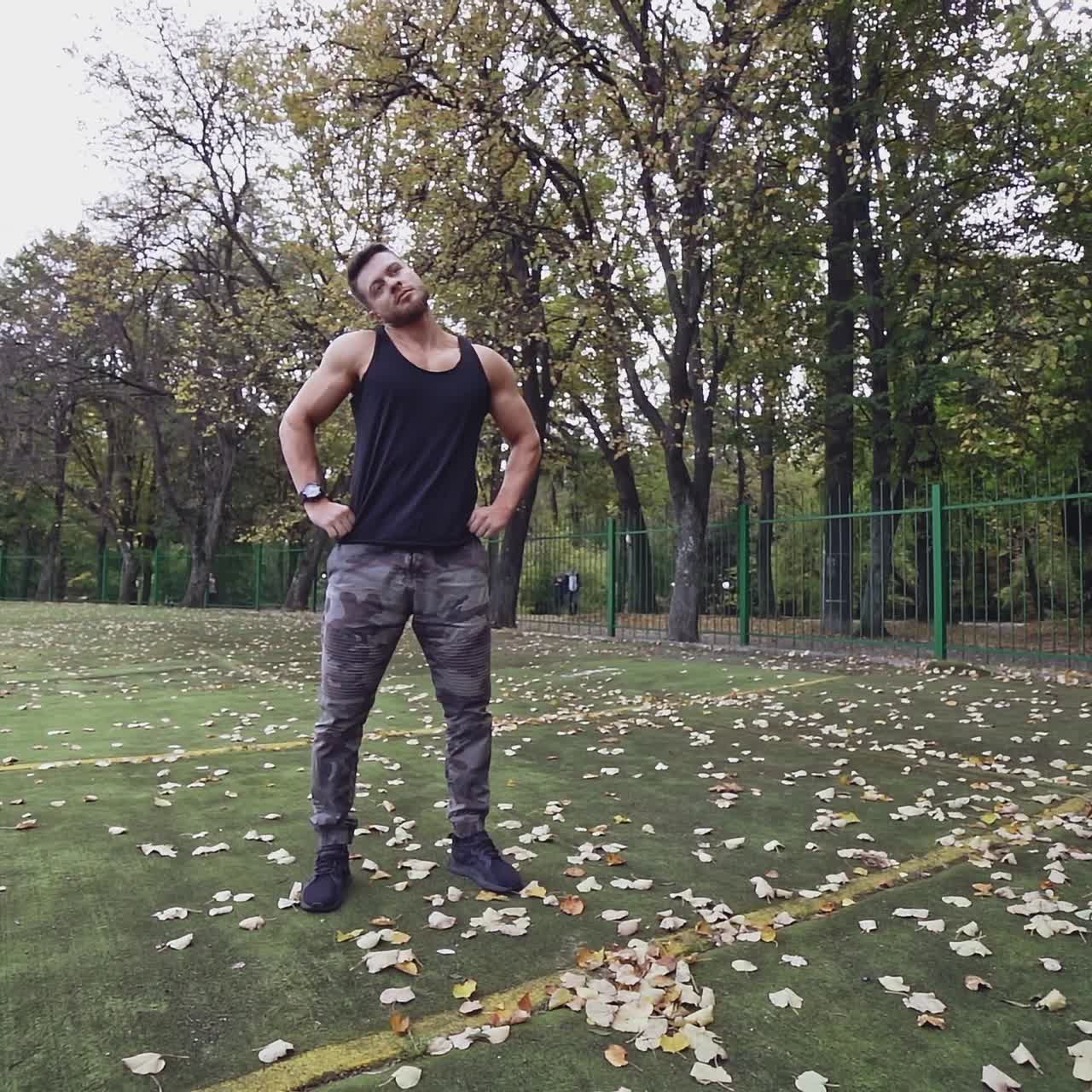 Muscular sportsman doing exercises in the open air. Strong athlete training his body on the stadium on nature background. Slow motion.
