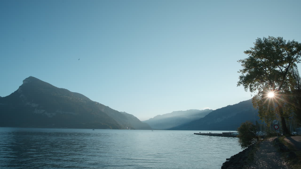 Naturskøn kystlinje med mole i Faulensee, Schweiz, med udsigt over morgendal mod solen.