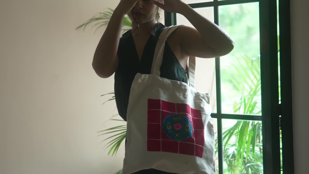 Kvinne som holder en fargerik veske innendørs, naturlig lys, rolig stemning.