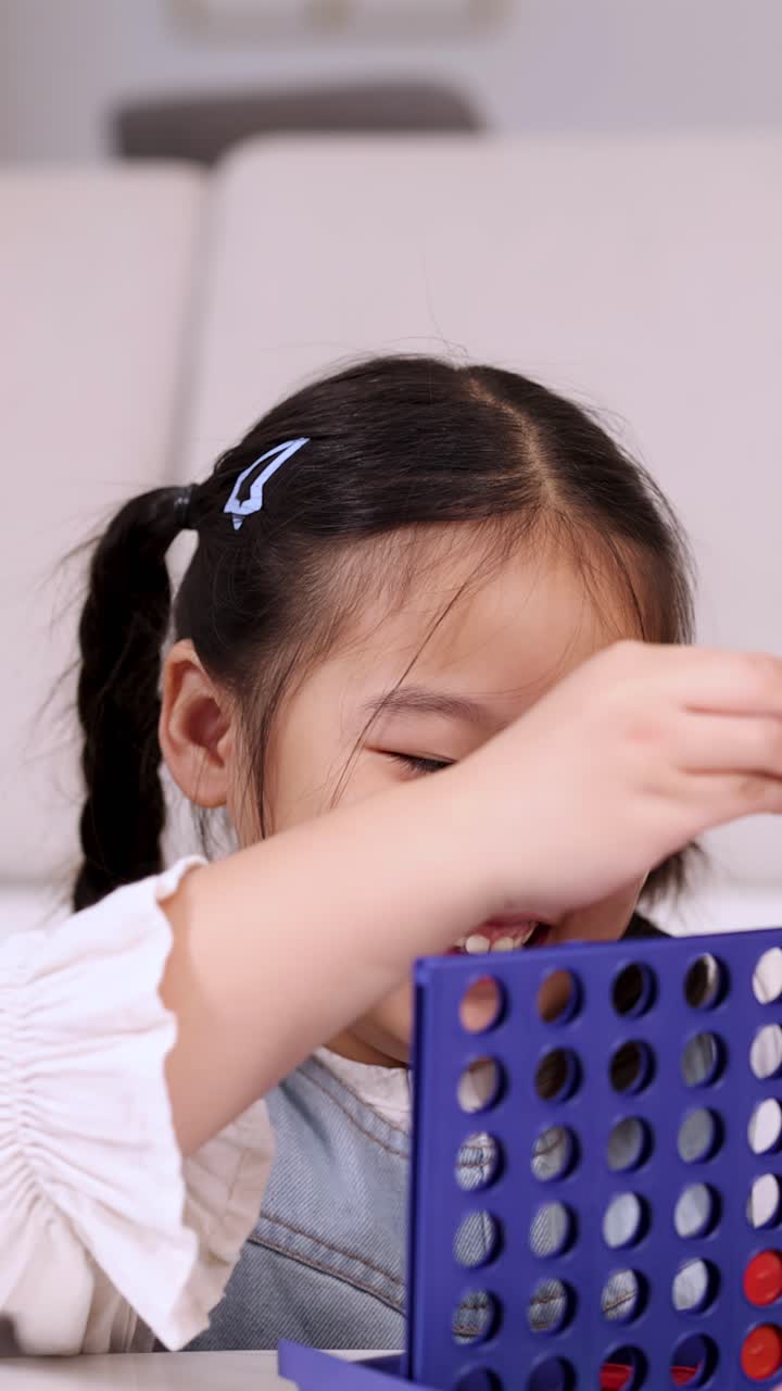 Smiling girl drops game pieces into Connect Four, bright indoor lighting, close-up, playful mood