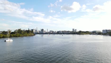 catamaran boats adrift on water surface of brisbane river with brisbane cbd skyline in distance