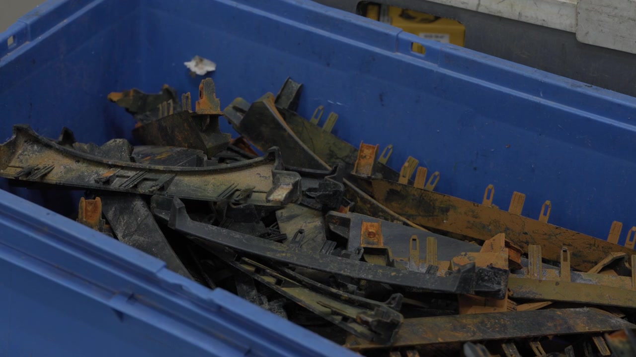 Corroded rusty automotive plastic and metal scrap parts piled in blue industrial recycling bin close up