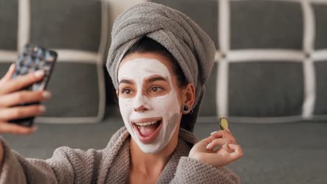 beautiful girl in a gray towel robe makes a selfie face in a clay mask