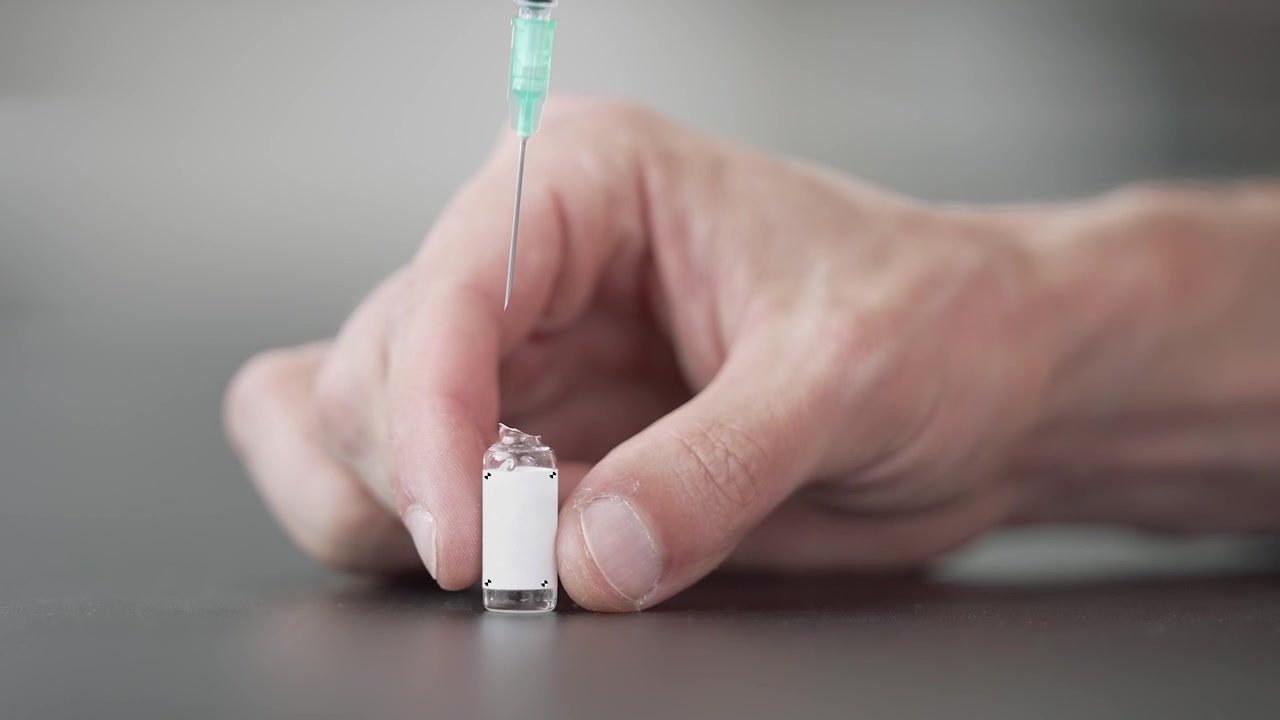 A blank ampoule with tracking markers stands on a table as a syringe needle goes in and starts drawing the liquid