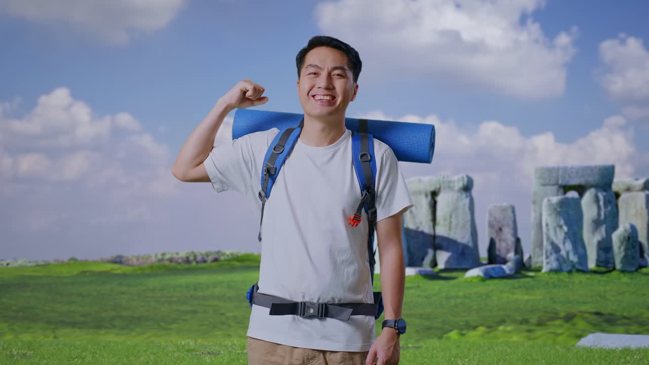 Asian Male Hiker With Mountaineering Backpack Smiling And Flexing His Bicep While Traveling In Stonehenge