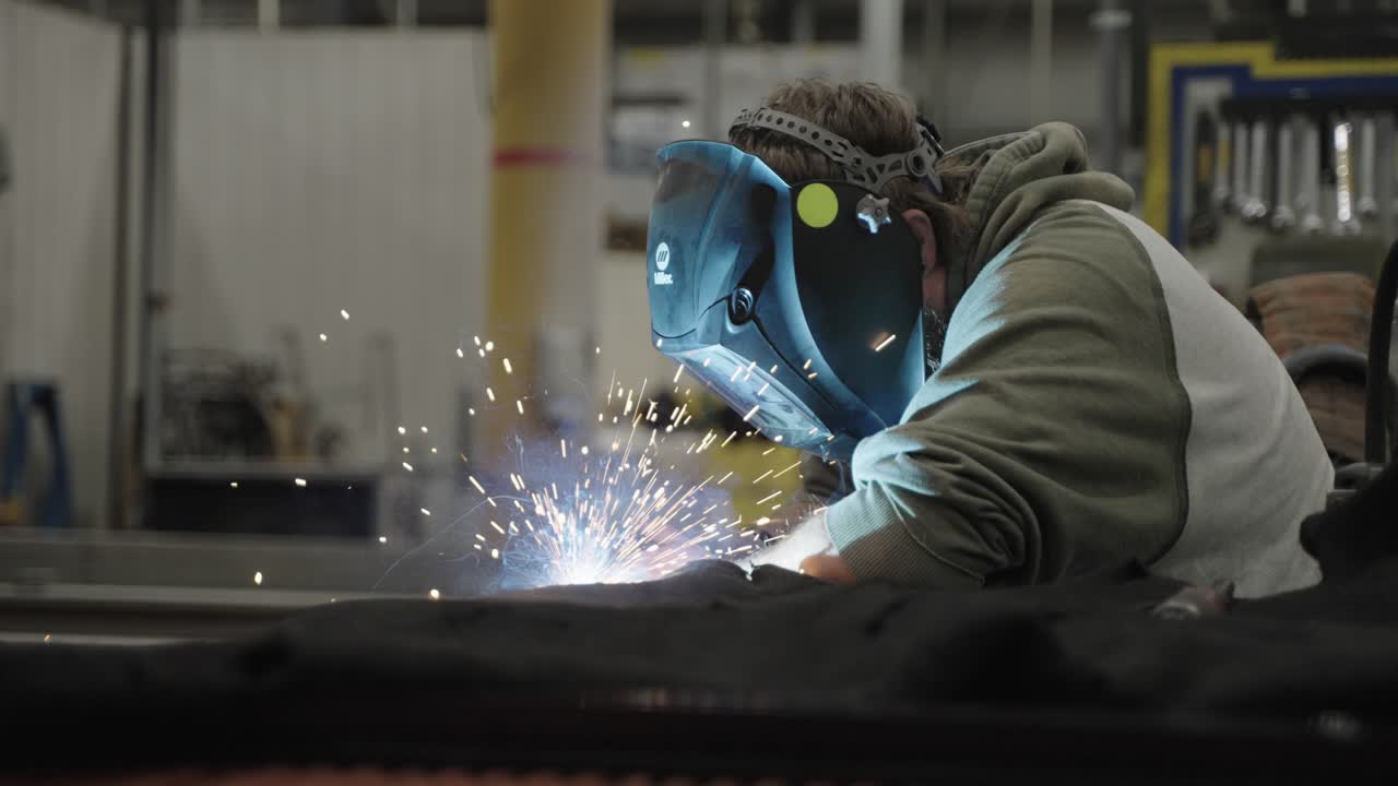 Worker wearing face shield welding metal, bright sparks flying in workshop