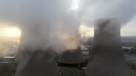 vista aérea izquierda del carro lento a través de las torres de refrigeración de la central eléctrica bajo las emisiones de vapor de humo al amanecer.
