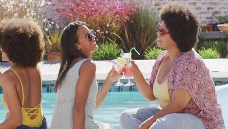 Happy-diverse-female-friends-making-toast-and-smiling-at-swimming-pool-party