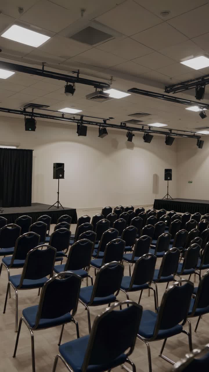 Wide-angle shot of an empty conference room with rows of chairs facing a stage, ready