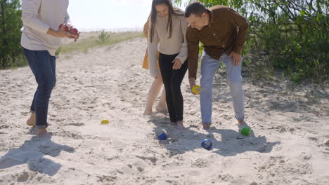 Gruppe-Von-Freundinnen-Und-Männern,-Die-An-Einem-Sonnigen-Tag-Petanque-Kugeln-Aus-Dem-Sand-Am-Strand-Holen