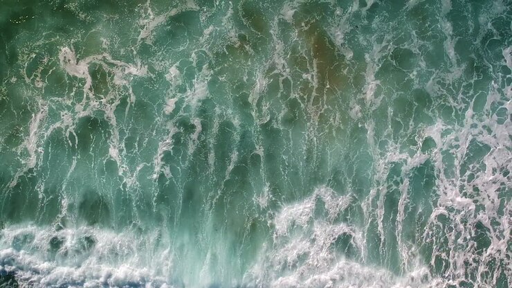 Drohnenaufnahme aus der Luft von Schaumkronenwellen, die an einem Strand in der Algarve, Portugal, hereinrollen.