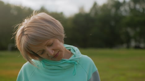 fair skinned lady in mint tracksuit performing chin tucks exercise outdoors on green field under cloudy sky during refreshing workout session promoting relaxation posture correction flexibility