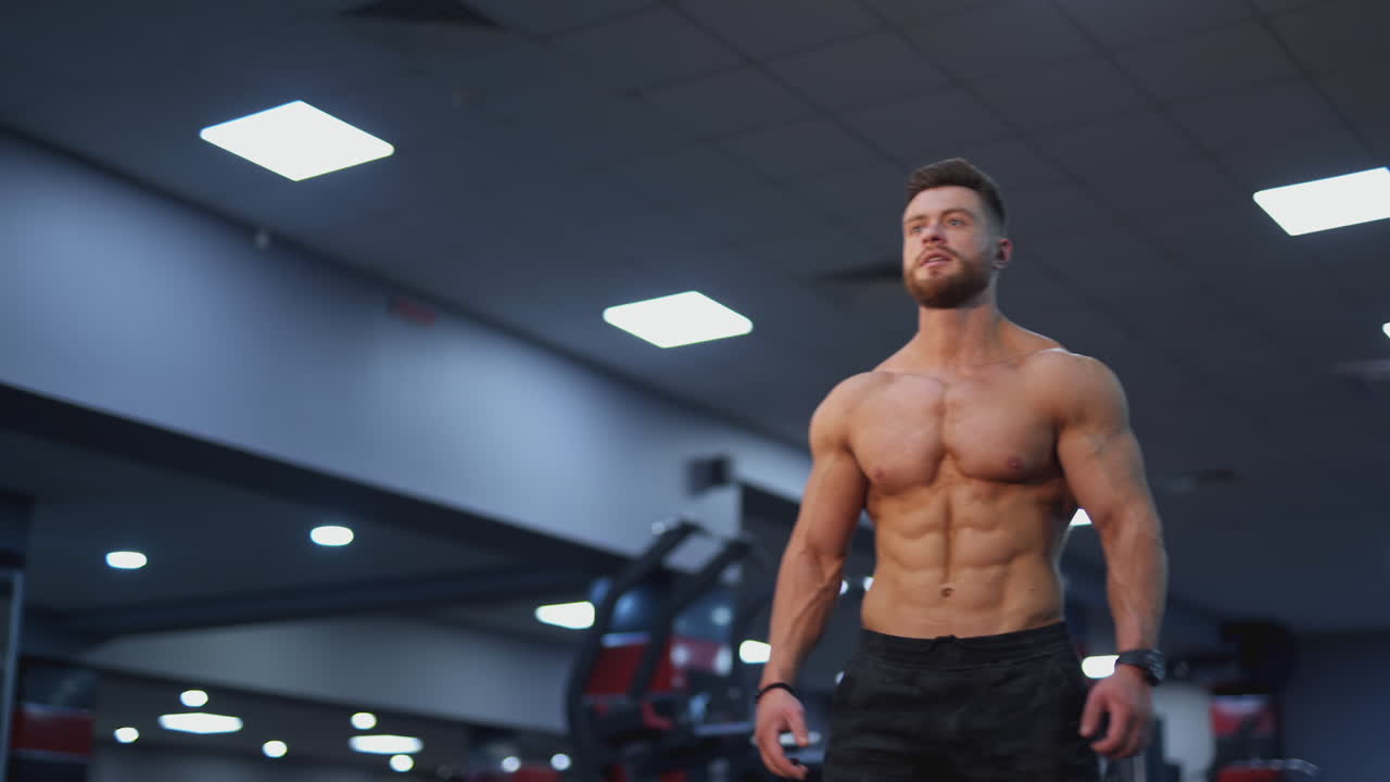 Sportsman with perfect muscular body in the gym. Young bodybuilder with naked torso stands in the gym and bothering his muscles. Sportive lifestyle.