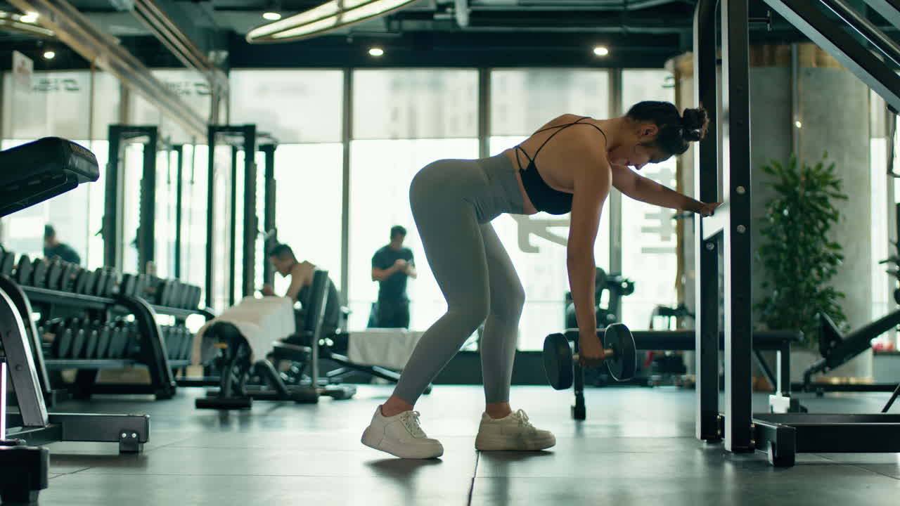 Asian girl doing dumbbell row for back workout standing in the fitness gym