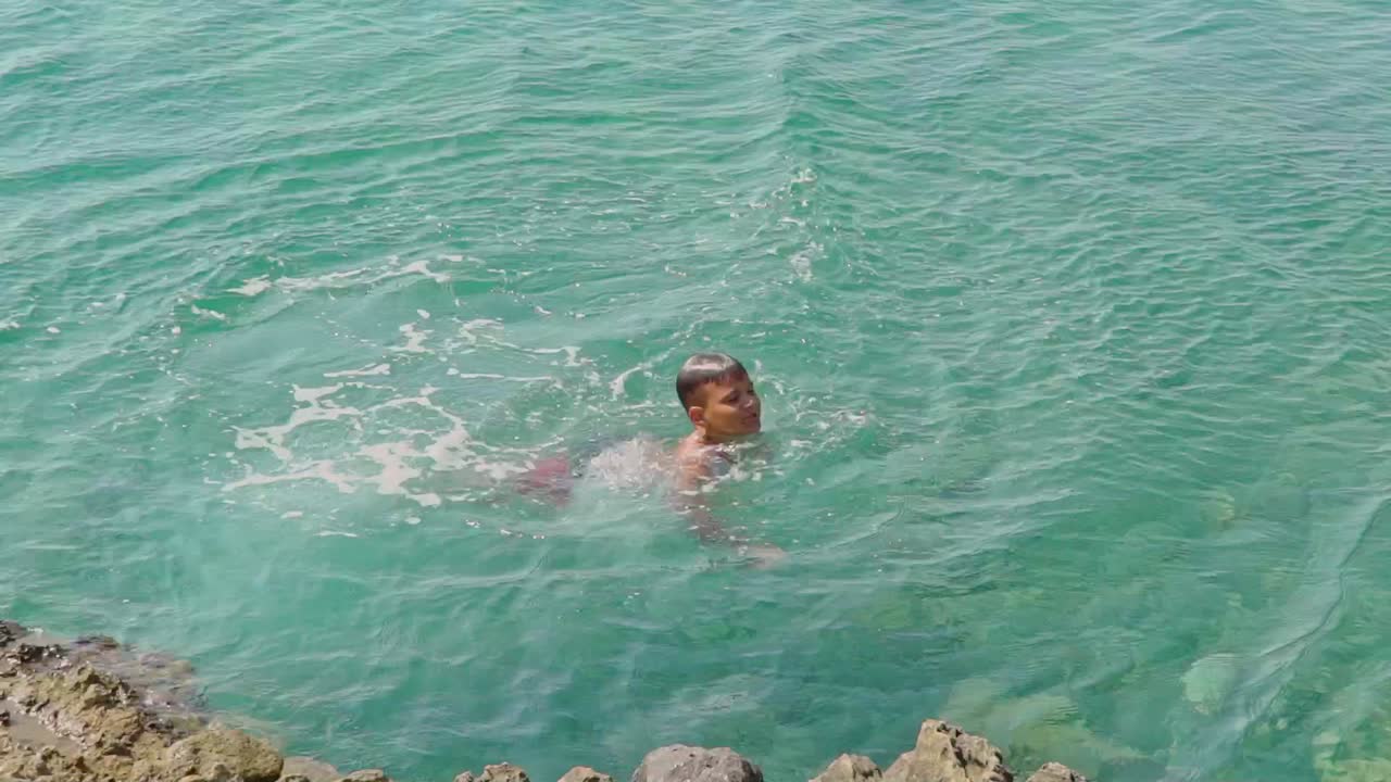 niño caucásico salta de una roca al mar, vista trasera 120fps
