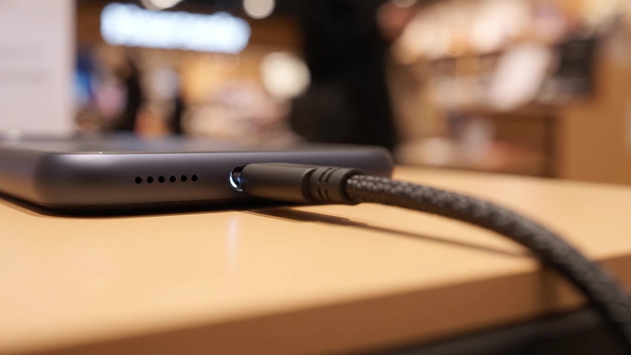 A close-up view showcasing a smartphone connected to a braided charging cable on a wooden table, emphasizing modern technology in a retail environment.