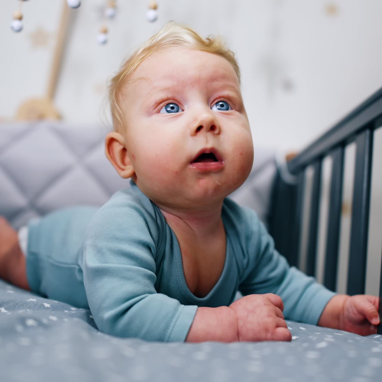 Bedårende blondt barn ligger fredfullt i barnesengen. Nydelig babyportrett som ligger på magen i krybben. Nærbilde.