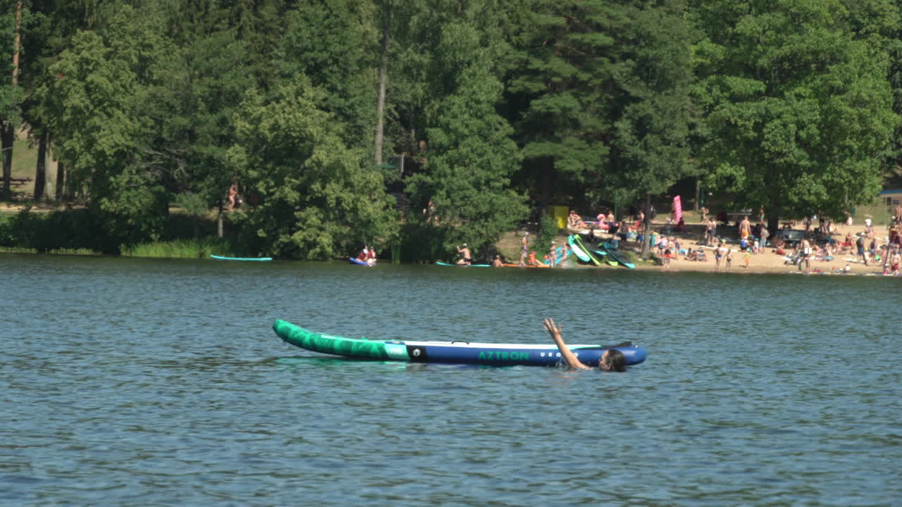 Girl swims in the lake. Sup board next to her. Beach background. Hot sunny summer day.