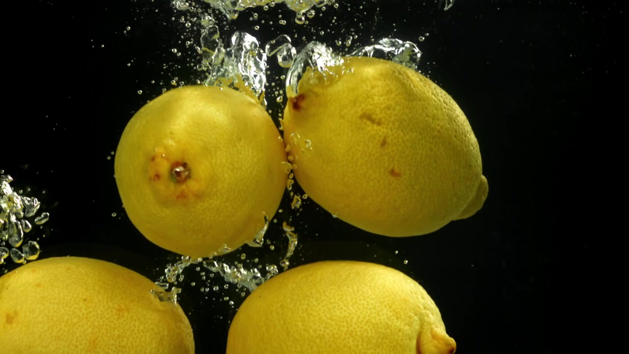 Limoni gialli freschi che cadono nell'acqua con bolle su sfondo nero