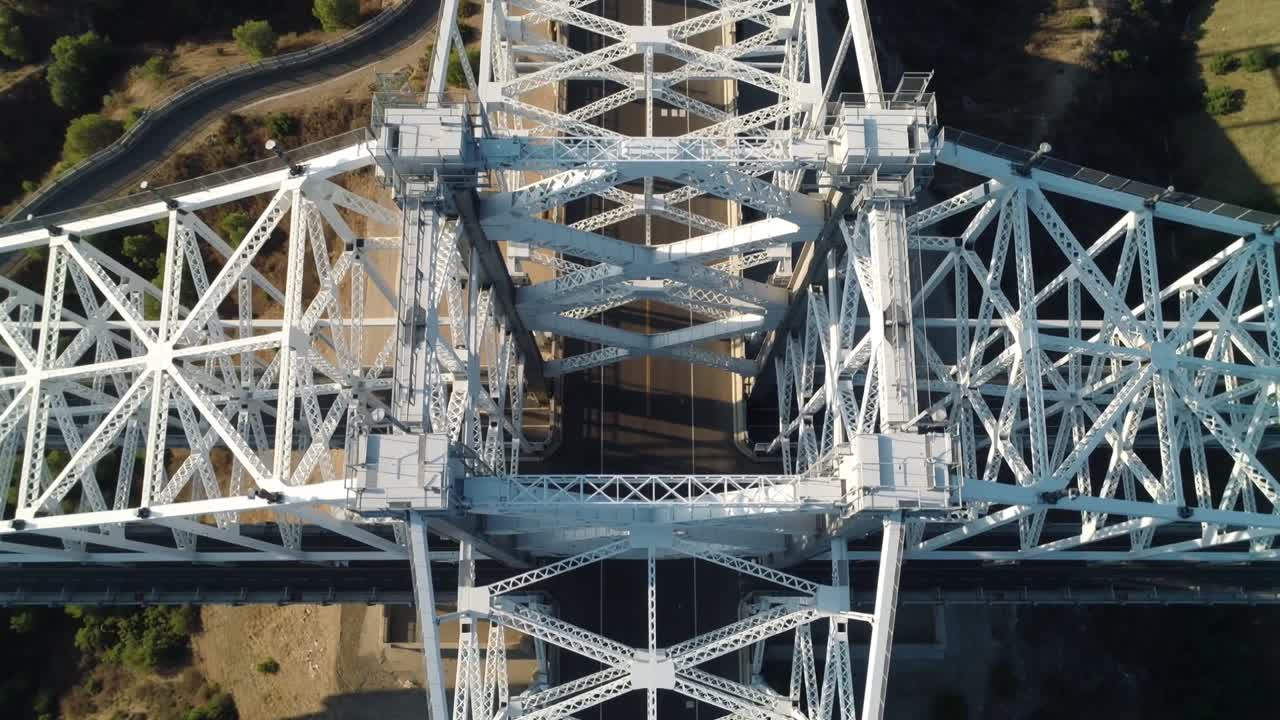 Descending drone capturing steel truss bridge over valley to show cross-bracing, casting shadows