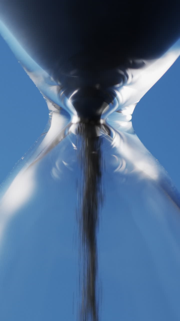 Vertical video of close up of hourglass with black sand pouring with copy space on blue background