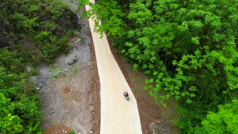 Drone-hovering-over-a-couple-riding-an-electric-scooter-and-heading-towards-a-tree-in-Yangshuo,-China