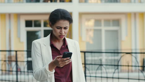 Mujer-Triste-Leyendo-El-Teléfono-Al-Aire-Libre.-Mujer-De-Negocios-Recibiendo-Malas-Noticias-En-La-Calle