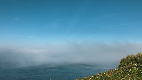 Fog-forming-over-sea,-camera-pans-right-showing-island-shrouded-in-fog-and-circular-rotation-of-sea-due-to-currents