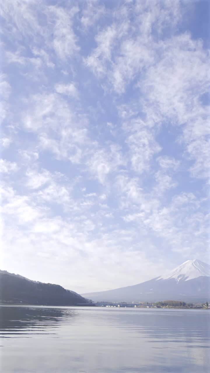 A breathtaking view of Mount Fuji surrounded by clear skies and floating clouds over Lake Kawaguchi shows nature's tranquil beauty as day breaks. Japan. Vertical video