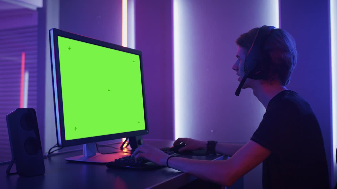Arc Sholt of the Pro Gamer Playing in Video Games on the Green Mock-up Screen on His Personal Computer. Talking with His Team through Microphone on Headphones. Retro Neon Room.