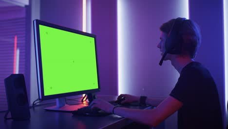 arc sholt of the pro gamer playing in video games on the green mock-up screen on his personal computer. talking with his team through microphone on headphones. retro neon room.