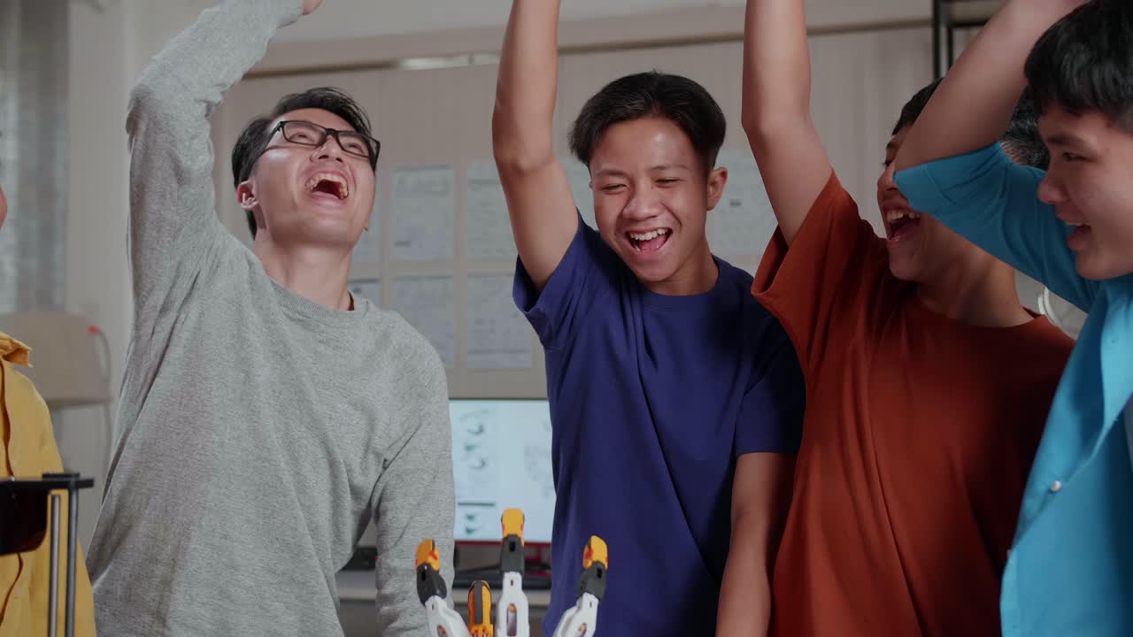 아시안 남자와 노트북과 3d 프린팅을 가진 소년들은 학교에서 사이보그 손에 대해 작업하는 동안 손을 함께 고 골을 외쳤다.