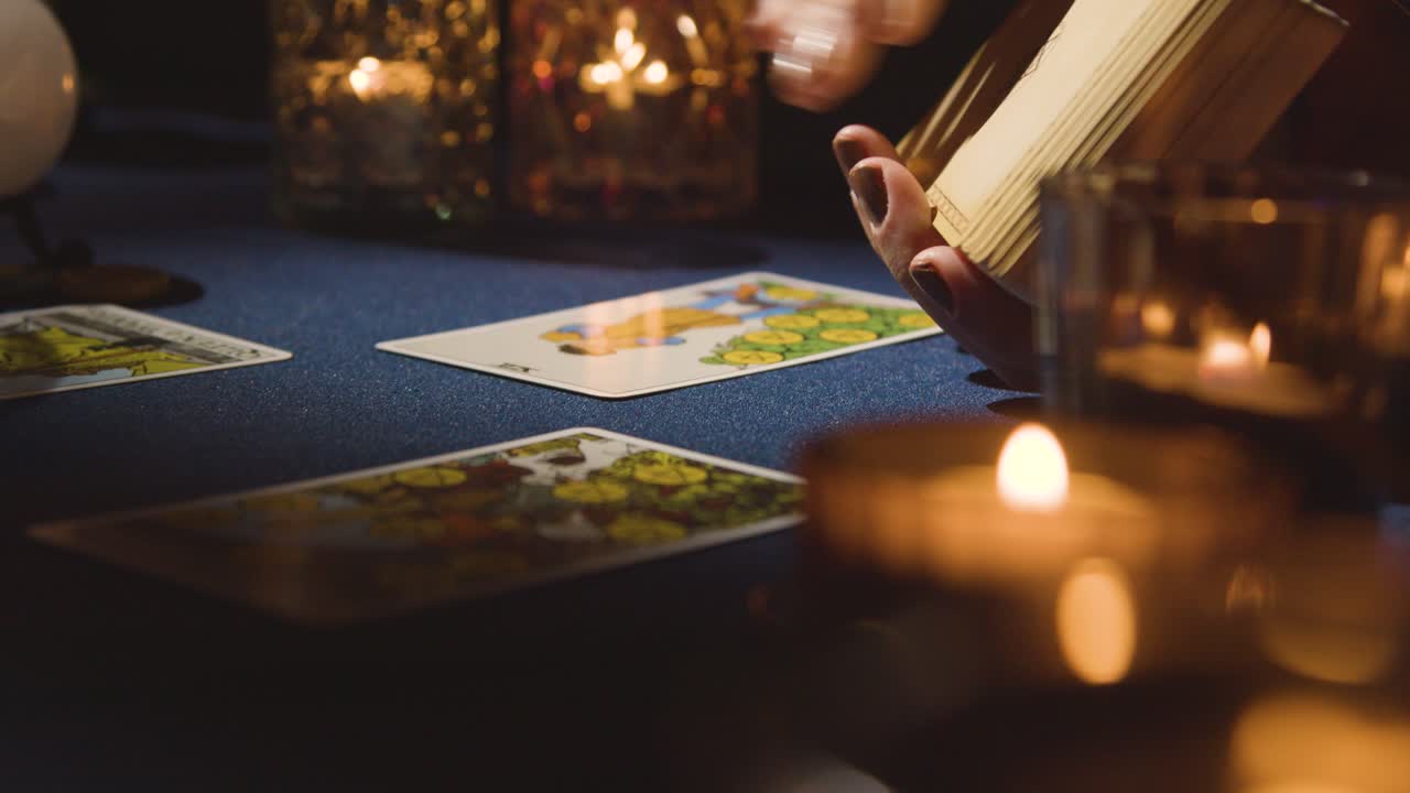 primer plano de una mujer dando una lectura de cartas del tarot en una mesa a la luz de las velas sosteniendo la carta de los amantes 2