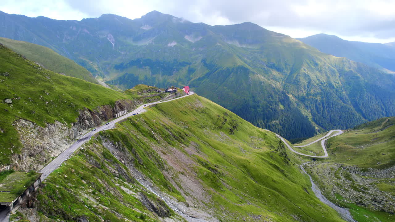 Aerial drone view of nature in Romania. Transfagarasan route in Carpathian mountains with moving cars visible through clouds, rocky slopes with greenery